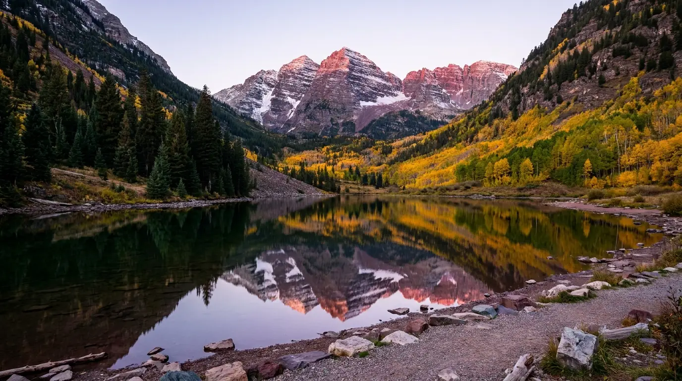 Two symmetrical dark maroon-hued fourteener peaks streaked with snow rising above a still alpine lake and golden autumn aspen, calm reflection at first light, Maroon Bells Elk Mountains Colorado, ultrarealistic photograph representative of the region