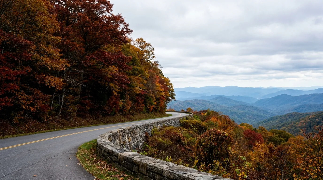 A two-lane mountain highway curving through dense hardwood forest high on a ridge with a stone overlook wall and vast blue-hazed layered ridges beyond, Newfound Gap Road Great Smoky Mountains National Park, ultrarealistic photograph representative of the region