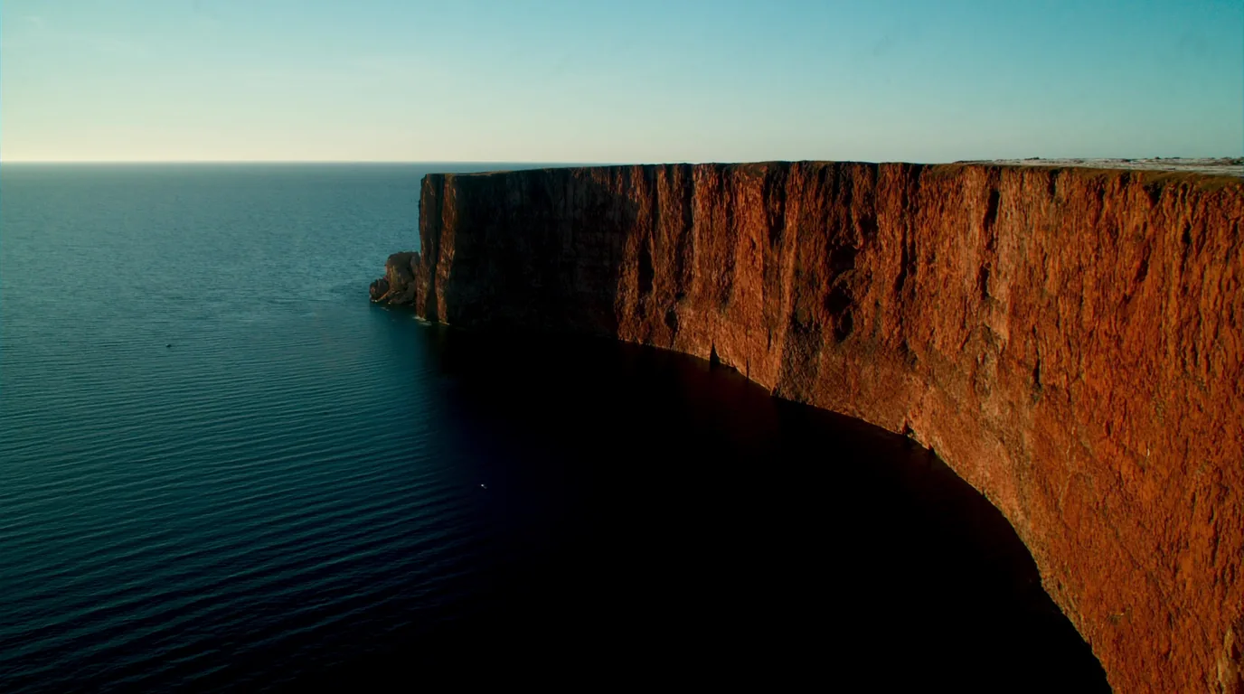 A high sheer basalt cliff dropping straight into the cold blue water of Lake Superior with conifer forest on the clifftop and a long open horizon, Minnesota North Shore, ultrarealistic photograph representative of the region