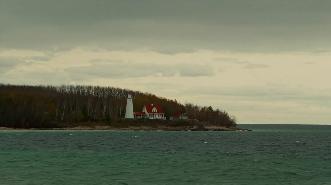 A white lighthouse and keeper buildings standing on a low wooded point beside Lake Superior with a pebble shoreline and open water beyond, Au Sable Light Station Michigan, ultrarealistic photograph representative of the region
