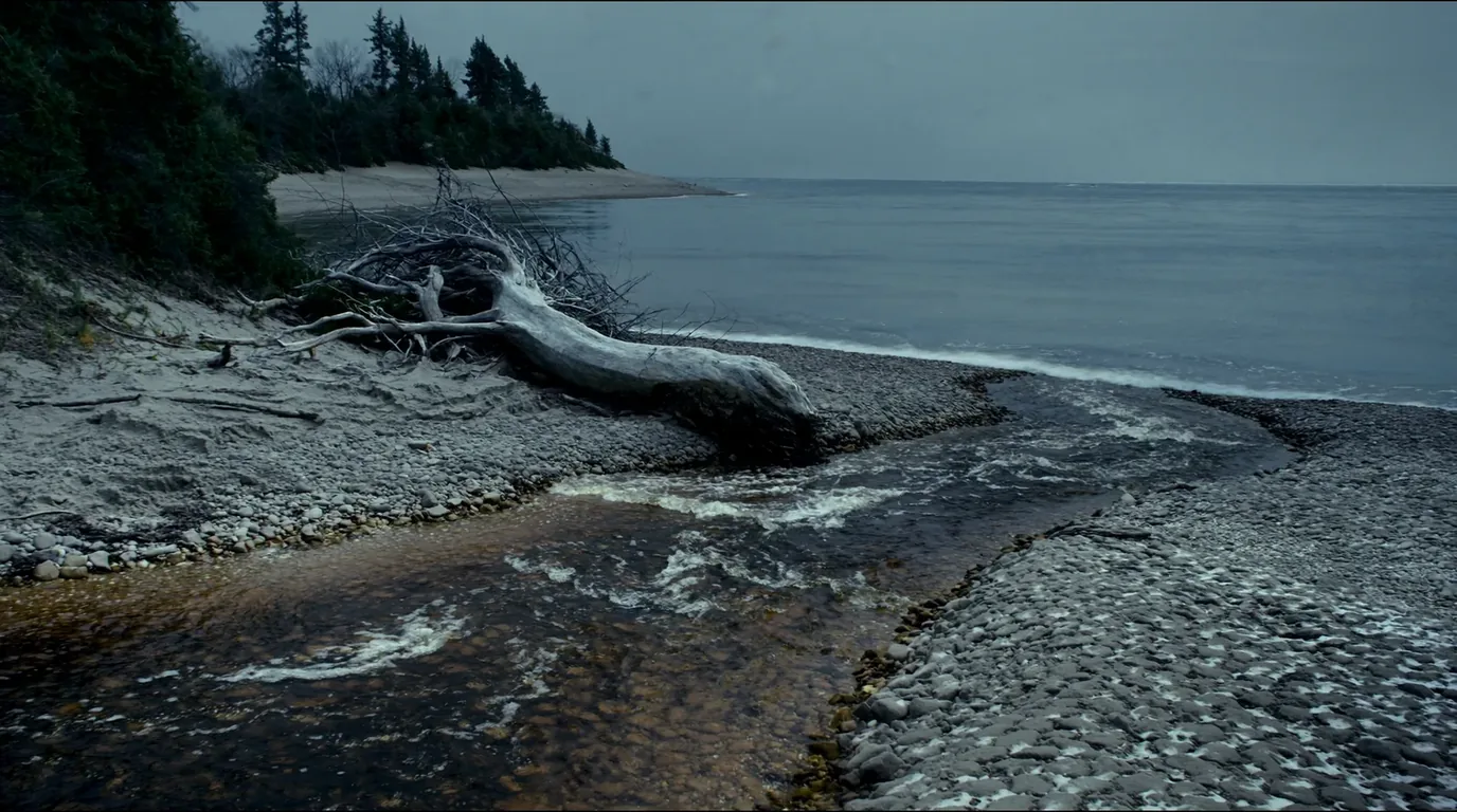 A tannin-dark river running out over cobbles into the clear cold water of Lake Superior with forest along both banks and an open lake horizon, Hurricane River Michigan, ultrarealistic photograph representative of the region