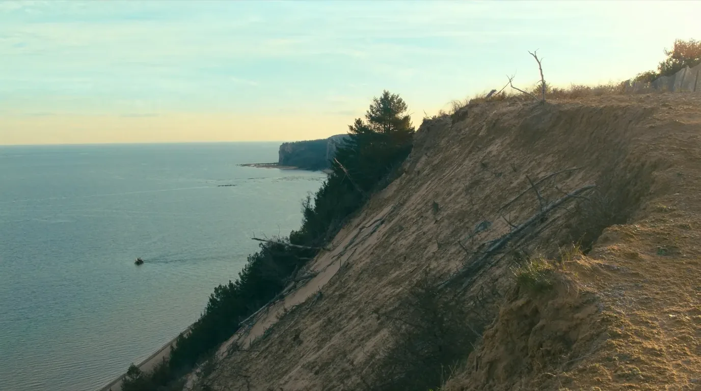 A steep slope of loose pale sand falling roughly three hundred feet from a wooded clifftop directly to the Lake Superior shoreline, viewed from the top, Michigan Upper Peninsula, ultrarealistic photograph representative of the region