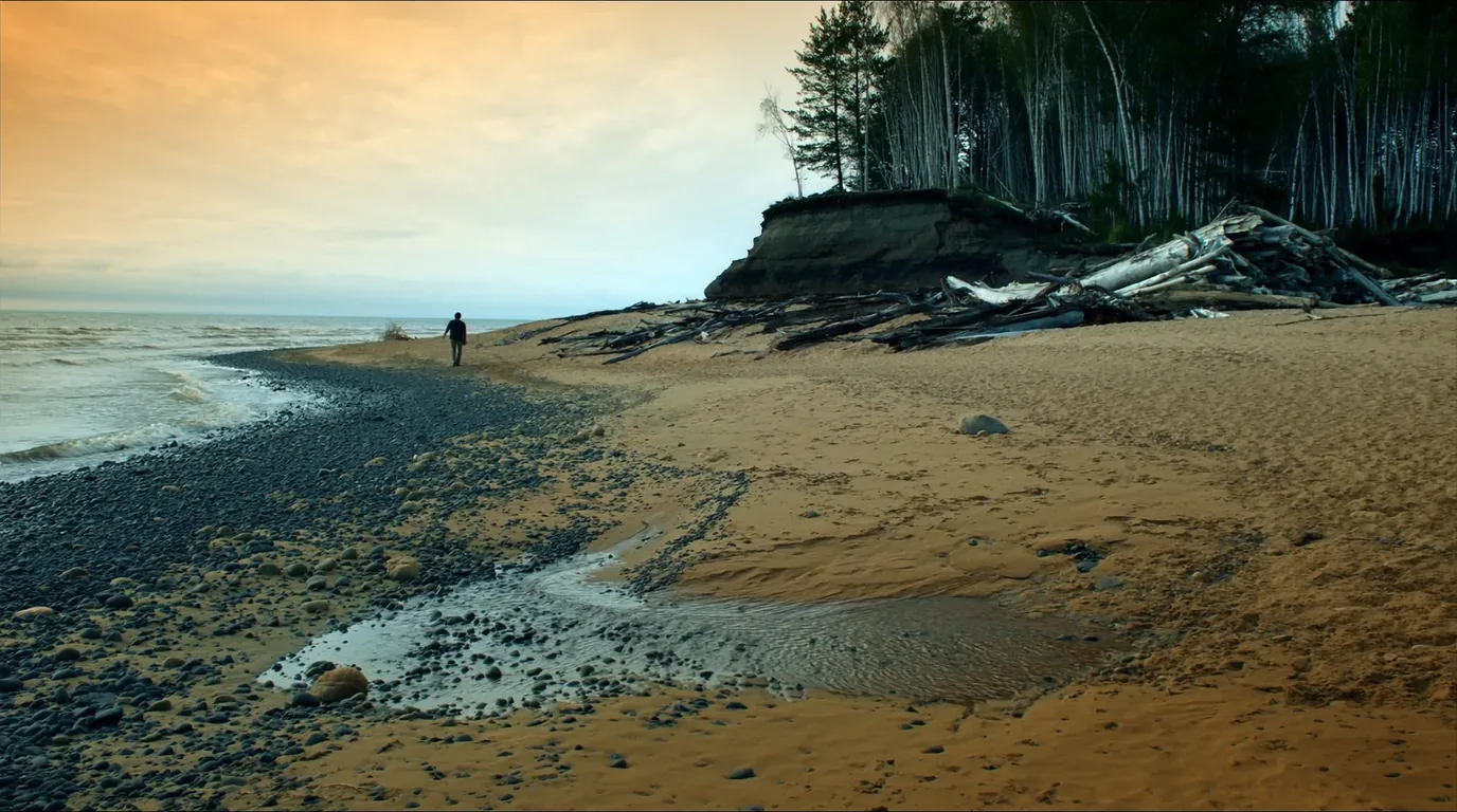 A long empty sand beach below low wooded bluffs on Lake Superior with clear shallow water and driftwood along the tideline, Pictured Rocks Michigan, ultrarealistic photograph representative of the region