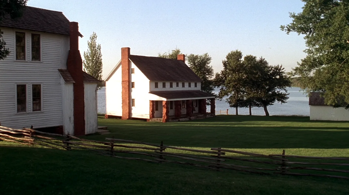 The restored 1844 army outpost at Fort Wilkins with white timber barracks buildings and a palisade beside a calm inland lake, dark forest behind, Copper Harbor Michigan, ultrarealistic photograph representative of the region