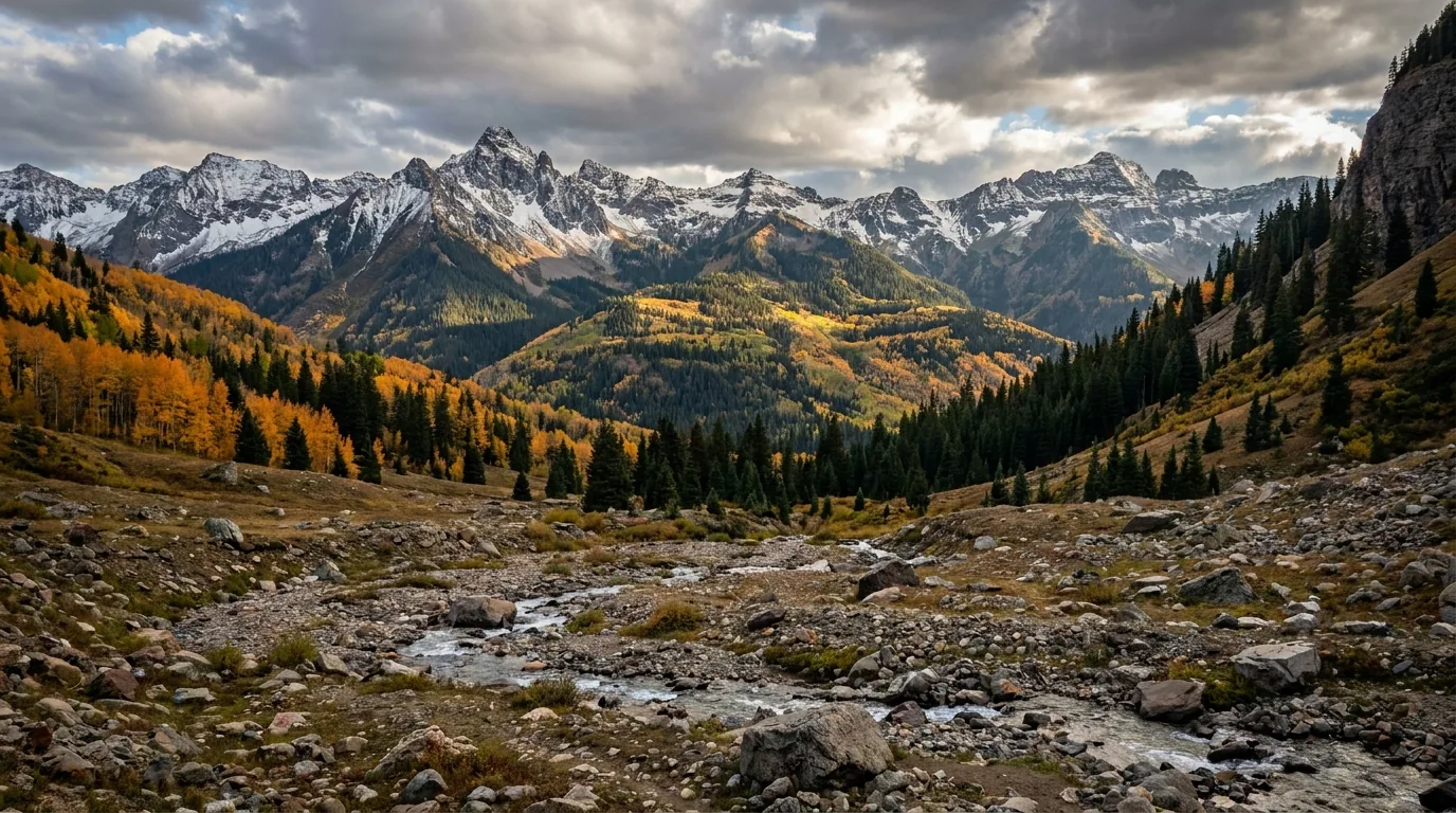 Jagged high alpine peaks above 13,000 feet with old mining roads cut across scree slopes, wildflower basins and a turquoise cirque lake below, warm late light, San Juan Mountains Colorado, ultrarealistic photograph representative of the region