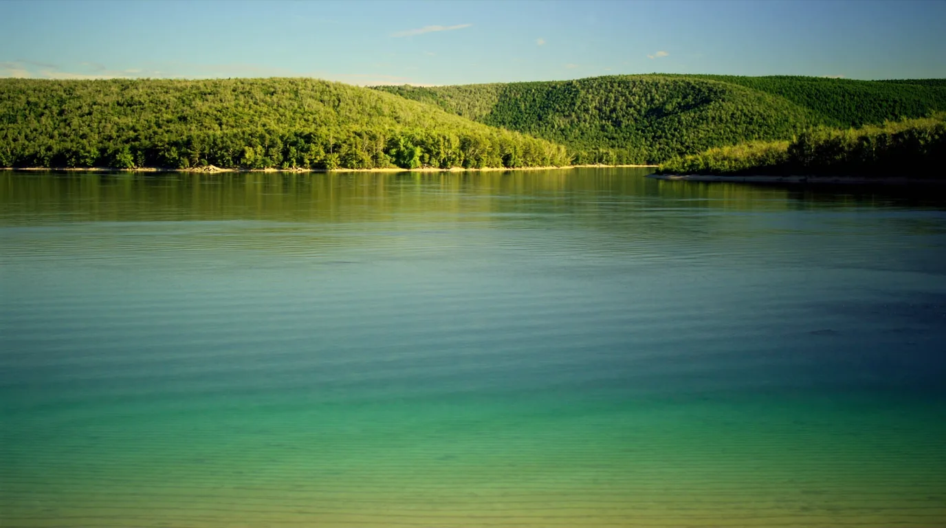 A startlingly turquoise inland lake seen from a wooded height with shallow pale sand bars visible through clear water and forested shoreline, Glen Lake northern Michigan, ultrarealistic photograph representative of the region