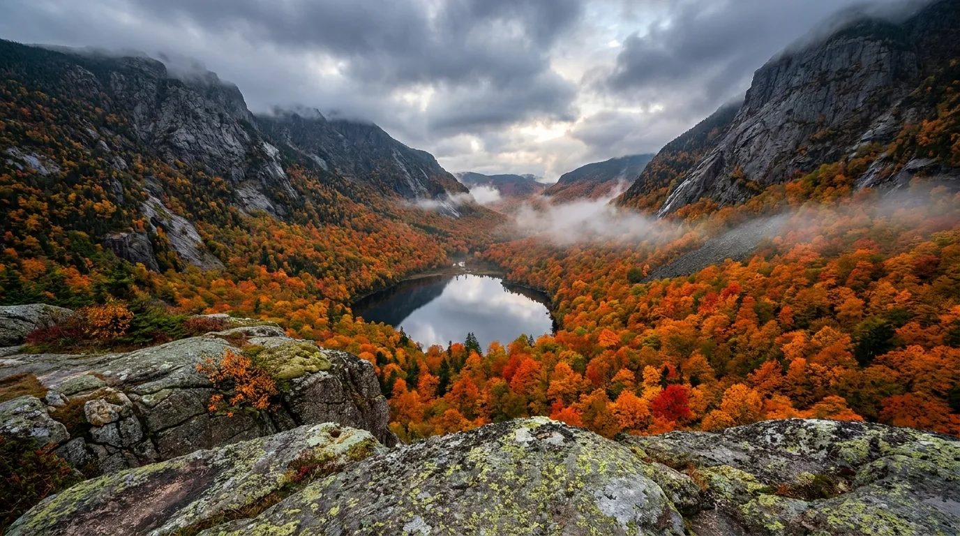 Looking down a deep glacier-cut notch valley from a low rocky ledge viewpoint at dawn, a small dark lake directly below surrounded by blazing autumn birch and maple forest with high mountain walls flanking the notch, the White Mountains of New Hampshire, ultrarealistic photograph representative of the region