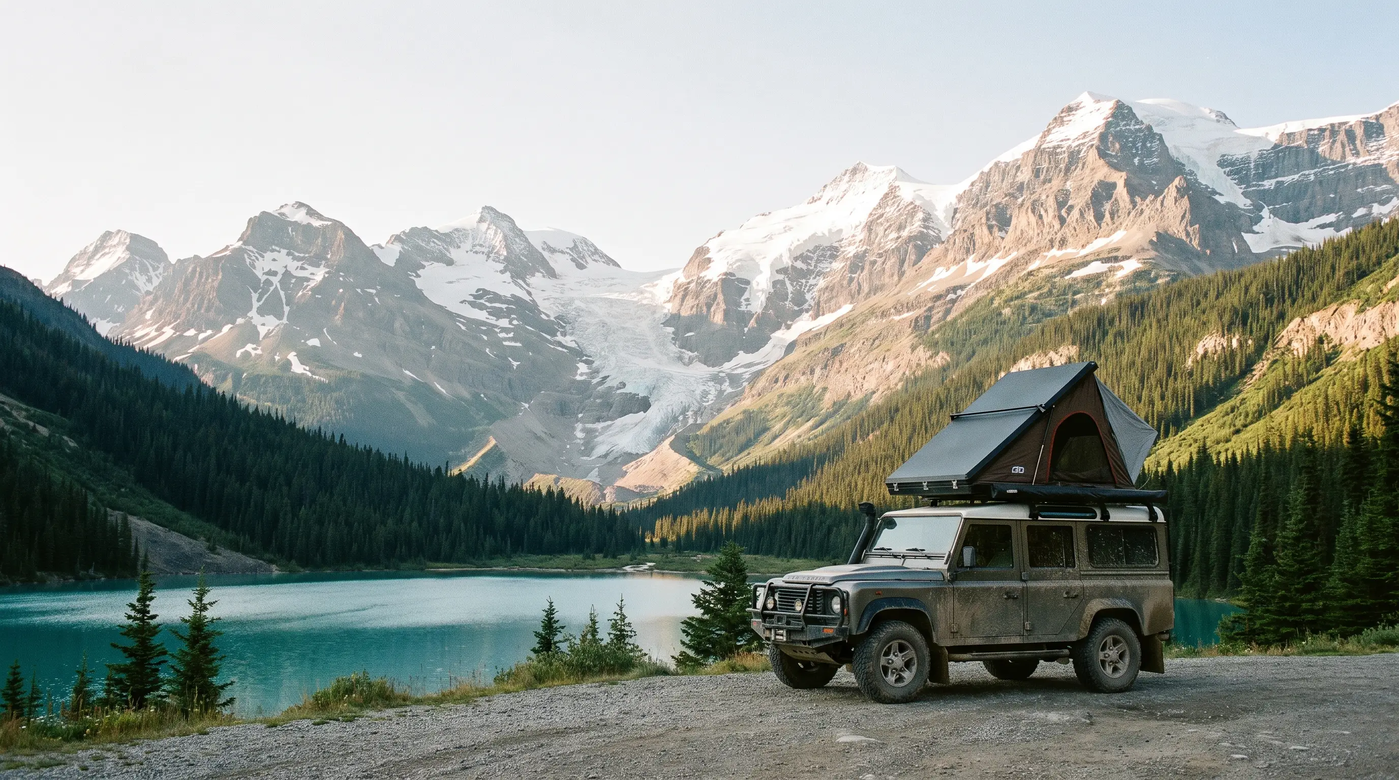 An overlanding rig with a rooftop tent parked at a gravel pullout beside a turquoise glacial lake on the Icefields Parkway, snow-capped Rockies behind.
